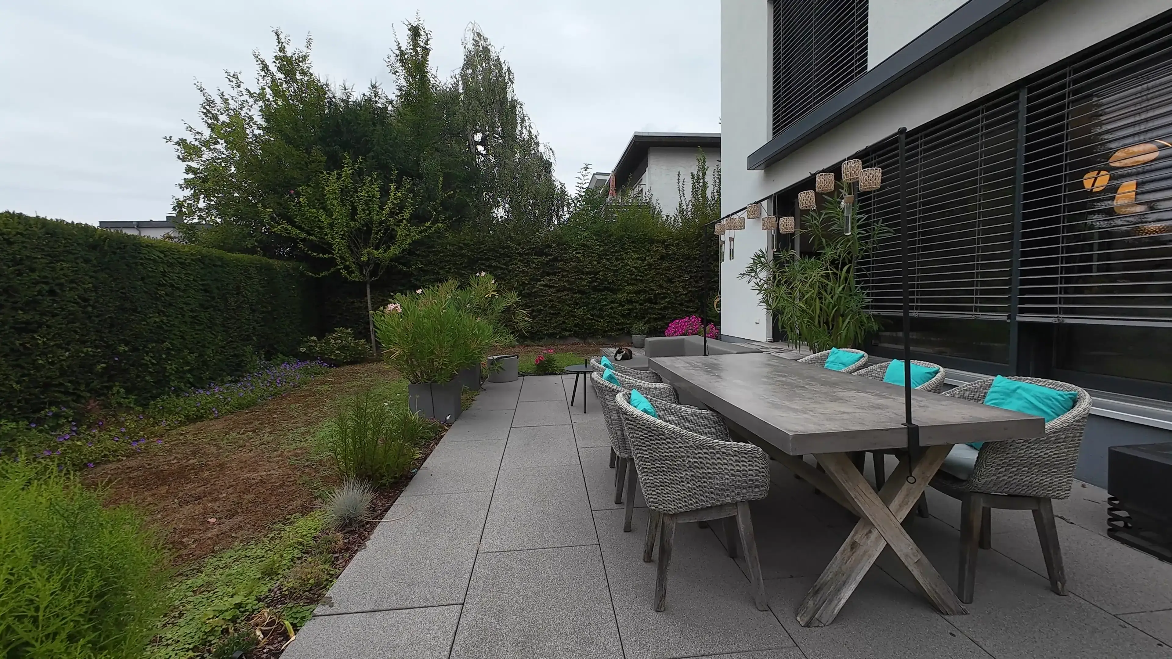 Flug von der Terrasse mit langem Esstisch ins Haus: Wohnraum mit Kamin und Klavier, dahinter die offene Küche mit Essplatz, am Ende die Diele mit Eichenparkett und offener Haustür.